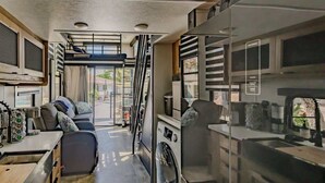 A compact RV interior with a kitchenette, a small seating area, and a washing machine.