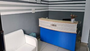 A reception desk with a blue base and a white top, a white sofa, and a small plant on the desk. - Pondy Pleasant Stay (Puducherry)