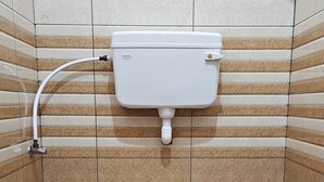 A bathroom with a toilet and a bidet, tiled walls, and a wooden floor. - Pondy Pleasant Stay (Puducherry)