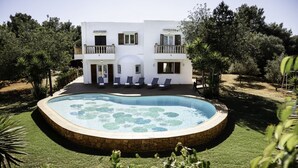 Una villa blanca con piscina rodeada de vegetación.