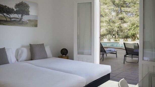 Un dormitorio con dos camas, un cuadro, una puerta que da a un balcón con piscina y sillas.