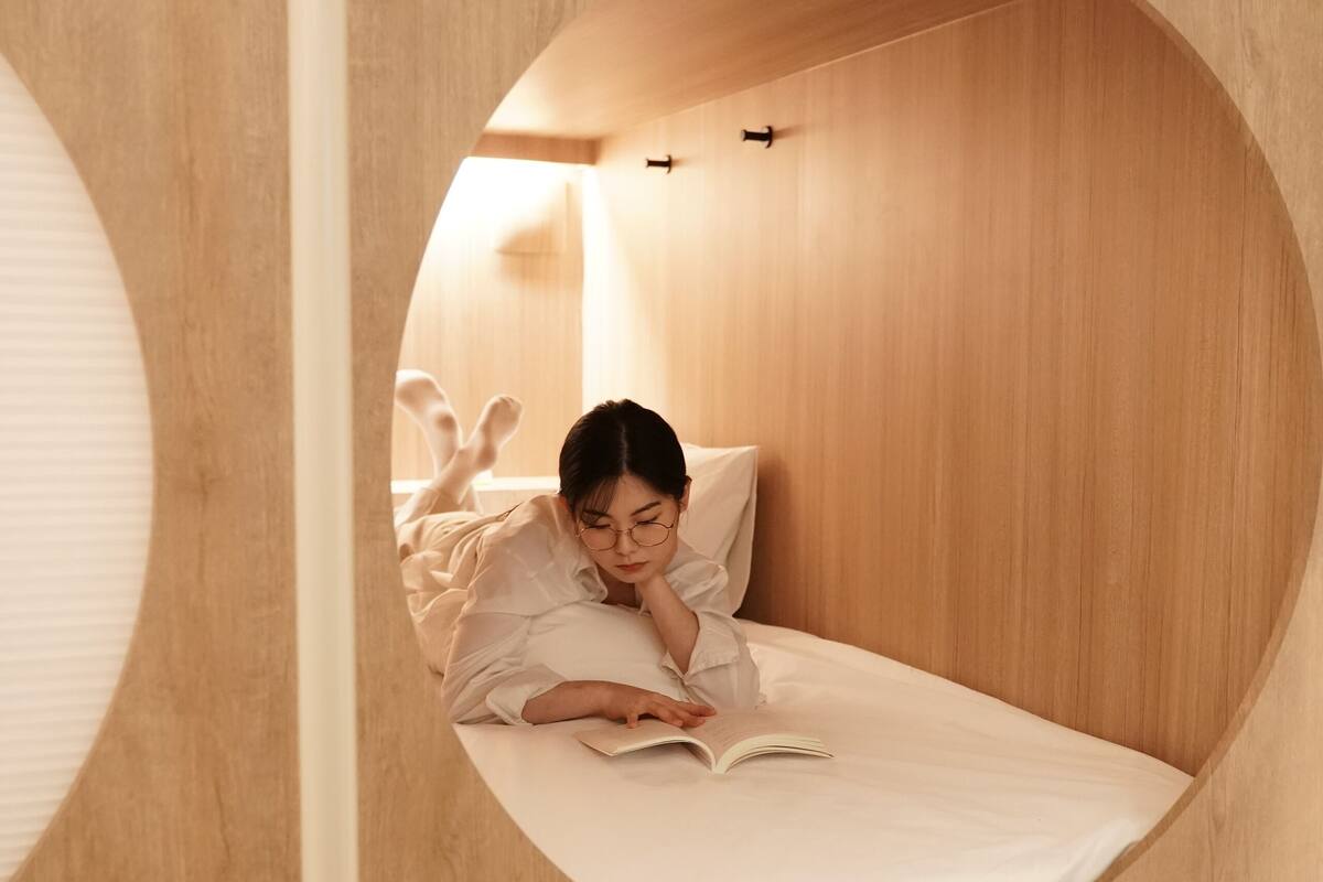A circular bunk bed with a person reading a book. The room has wooden walls and a white ceiling.