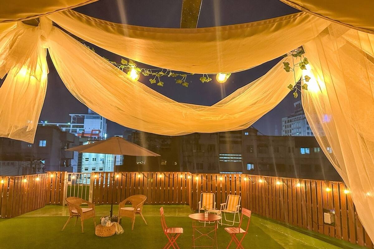 An outdoor seating area with a wooden fence, string lights, and draped fabric.