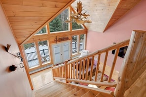 Interior de madera con una escalera, ventanas amplias y vistas al exterior.