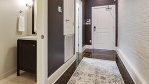 Un pasillo con una pared oscura, una puerta blanca, un timbre blanco y un mueble pequeño y oscuro.