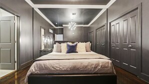 Un dormitorio con una cama grande, suelo de madera oscura y una araña.