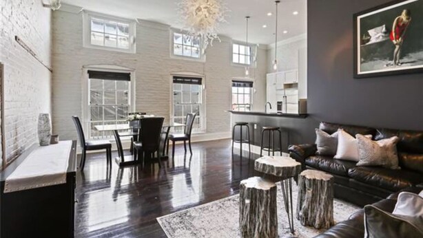 Una sala de estar moderna con un sofá de cuero oscuro, una zona de comedor con una mesa y sillas, y una cocina al fondo.