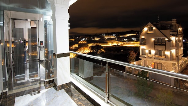A balcony with a glass railing overlooking a lit-up building at night. - Japan Villa Homestay ByTheHill (Lam Vien - Da Lat)