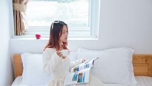 A person sitting on a bed with a magazine, a cup, and an apple on the windowsill. - Japan Villa Homestay ByTheHill (Lam Vien - Da Lat)