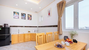 A modern kitchen with wooden cabinets, a dining table set with plates, cups, and a kettle. - Japan Villa Homestay ByTheHill (Lam Vien - Da Lat)