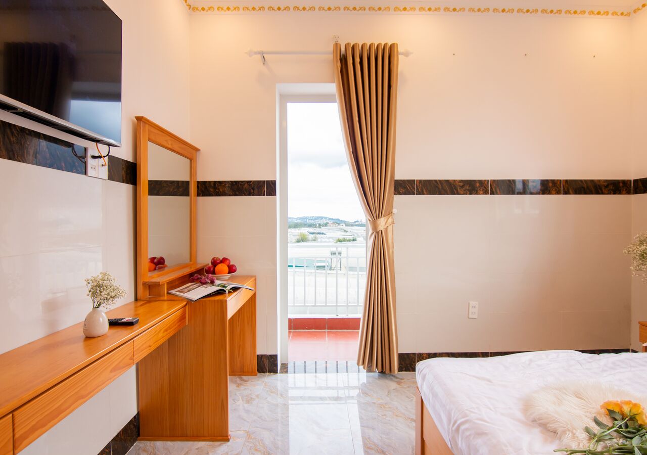 A hotel room with a wooden desk, a mirror, a bed, and a balcony with a view.