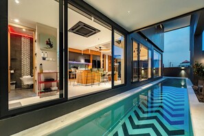 A modern house with a swimming pool, large windows, and a kitchen visible through the glass doors. - Beautiful Sea View Full Smart House 3BR (Rawai)