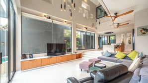 A modern living room with a large TV, comfortable seating, and a staircase leading to an upper level. - Beautiful Sea View Full Smart House 3BR (Rawai)