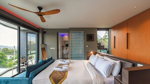 A modern hotel room with a large bed, a ceiling fan, a view of the outdoors, and a balcony with seating. - Beautiful Sea View Full Smart House 3BR (Rawai)