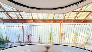 A corner room with a curved ceiling, two wicker chairs, a small table, a woven rug, and a white vase with dried plants.