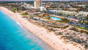 An aerial view of a coastal resort with a beach, a large hotel, and a pool area.