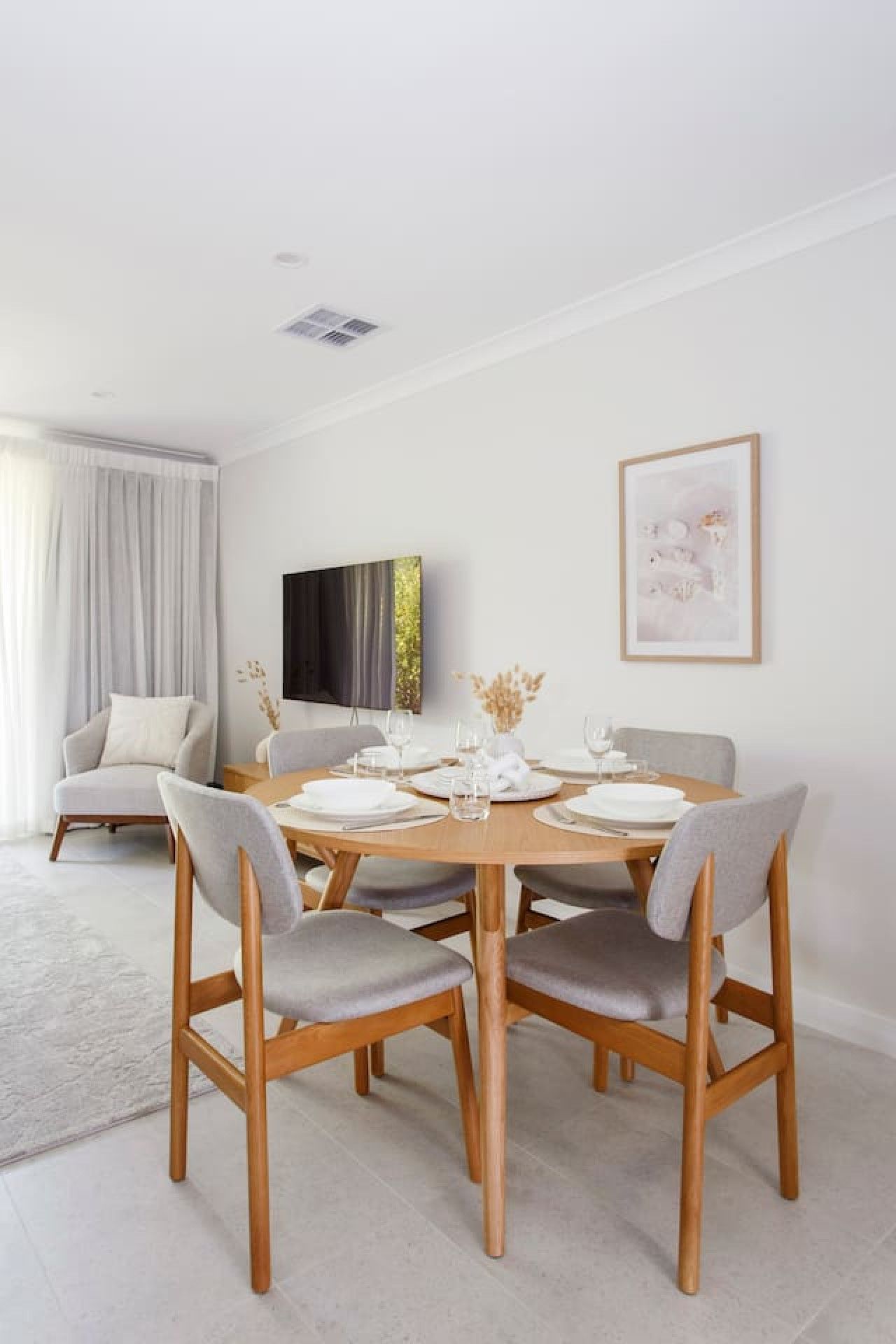 A modern dining room with a round wooden table set for four, surrounded by grey upholstered chairs.