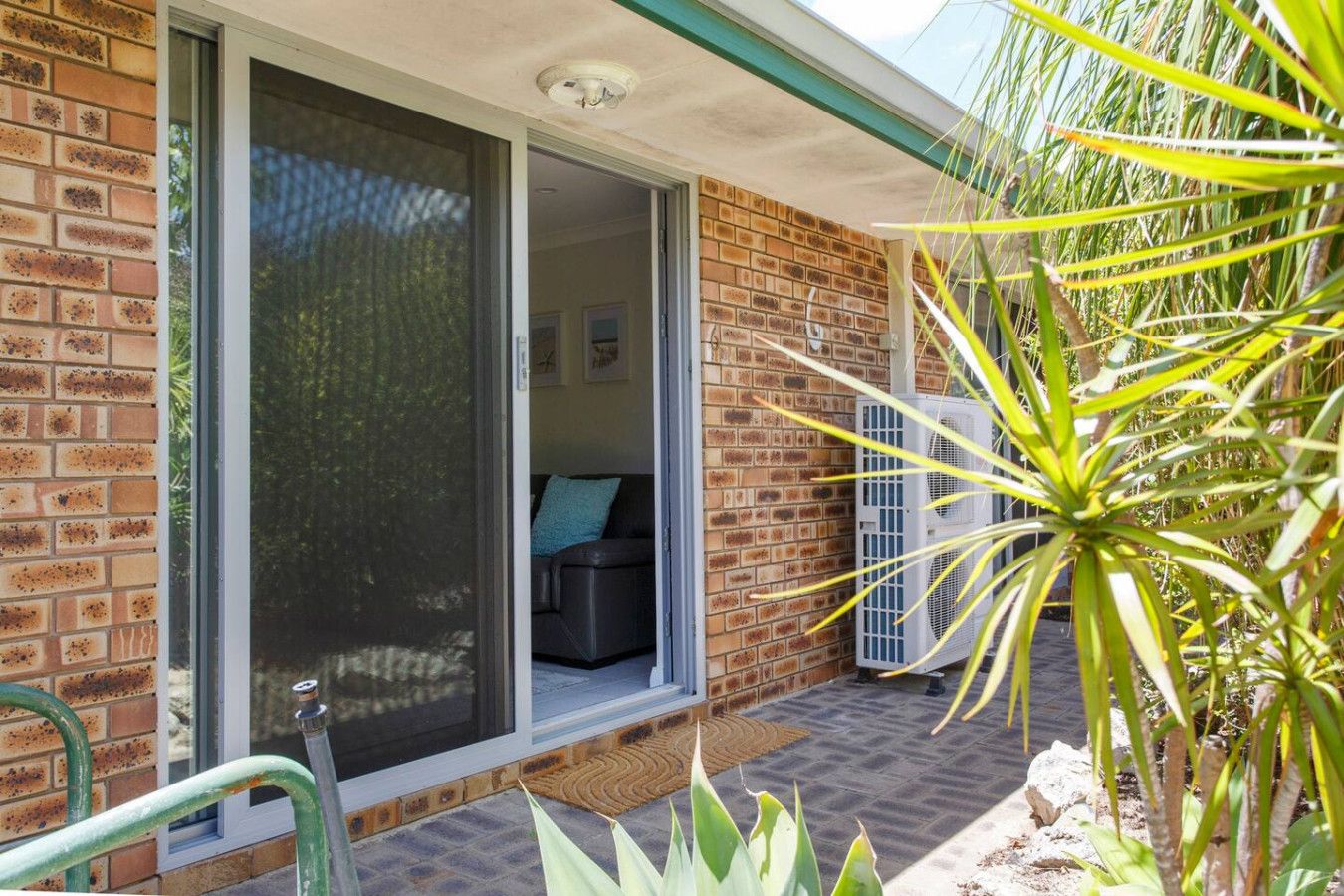 A brick house with a sliding glass door leading to a living area with a couch and an air conditioning unit.