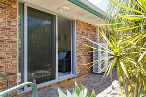 A brick house with a sliding glass door leading to a living area with a couch and an air conditioning unit. - Maylands Riverside City Retreat (Maylands)