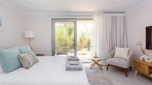 A modern bedroom with a large bed, a chair, a small table, and a view of greenery outside. - Maylands Riverside City Retreat (Maylands)