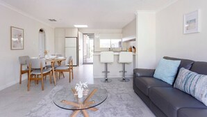 A modern living room with a grey sofa, a glass coffee table, and a dining area with wooden chairs and a white table. - Maylands Riverside City Retreat (Maylands)