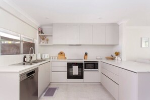 A compact kitchen with white cabinetry, a dishwasher, a microwave, and a sink. - Maylands Riverside City Retreat (Maylands)