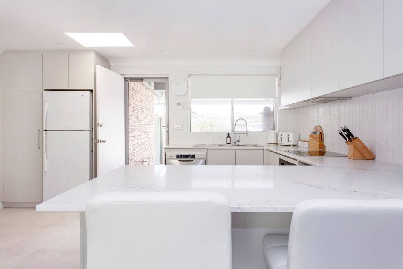 Una cocina moderna con armarios blancos, encimera de mármol y horno empotrado.