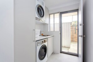 A compact laundry area with a washing machine, dryer, and a small countertop with a sink. - Maylands Riverside City Retreat (Maylands)