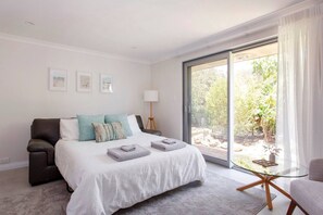 A bedroom with a bed, a chair, a lamp, and a view of the outdoors.