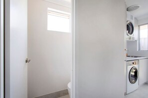 A laundry room with a washing machine and dryer, a small window, and a door. - Maylands Riverside City Retreat (Maylands)