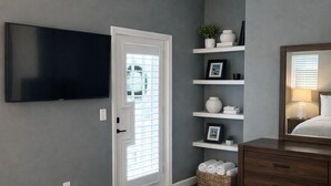 Una camera da letto con un letto, una TV, una ventola a soffitto, una cassettiera e uno scaffale con oggetti decorativi.