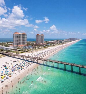 Una playa con un muelle, aguas turquesas cristalinas y una fila de hoteles al fondo.