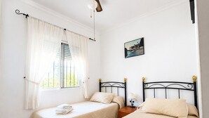 A bedroom with two beds, a window with curtains, a wall-mounted picture, and a bedside table with a lamp. - 1213 Cortijo del Rey (Frigiliana)