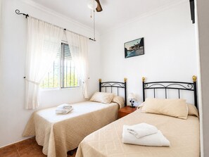 A bedroom with two beds, a window with curtains, a wall-mounted picture, and a bedside table with a lamp. - 1213 Cortijo del Rey (Frigiliana)