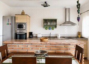 A kitchen with a brick island, a microwave, a stove, a coffee maker, and a hanging light fixture. - 1213 Cortijo del Rey (Frigiliana)