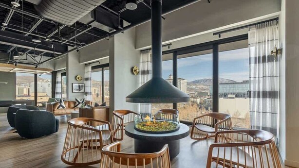 Un salon moderne doté d’un foyer central, de grandes fenêtres et offrant une vue sur la ville.