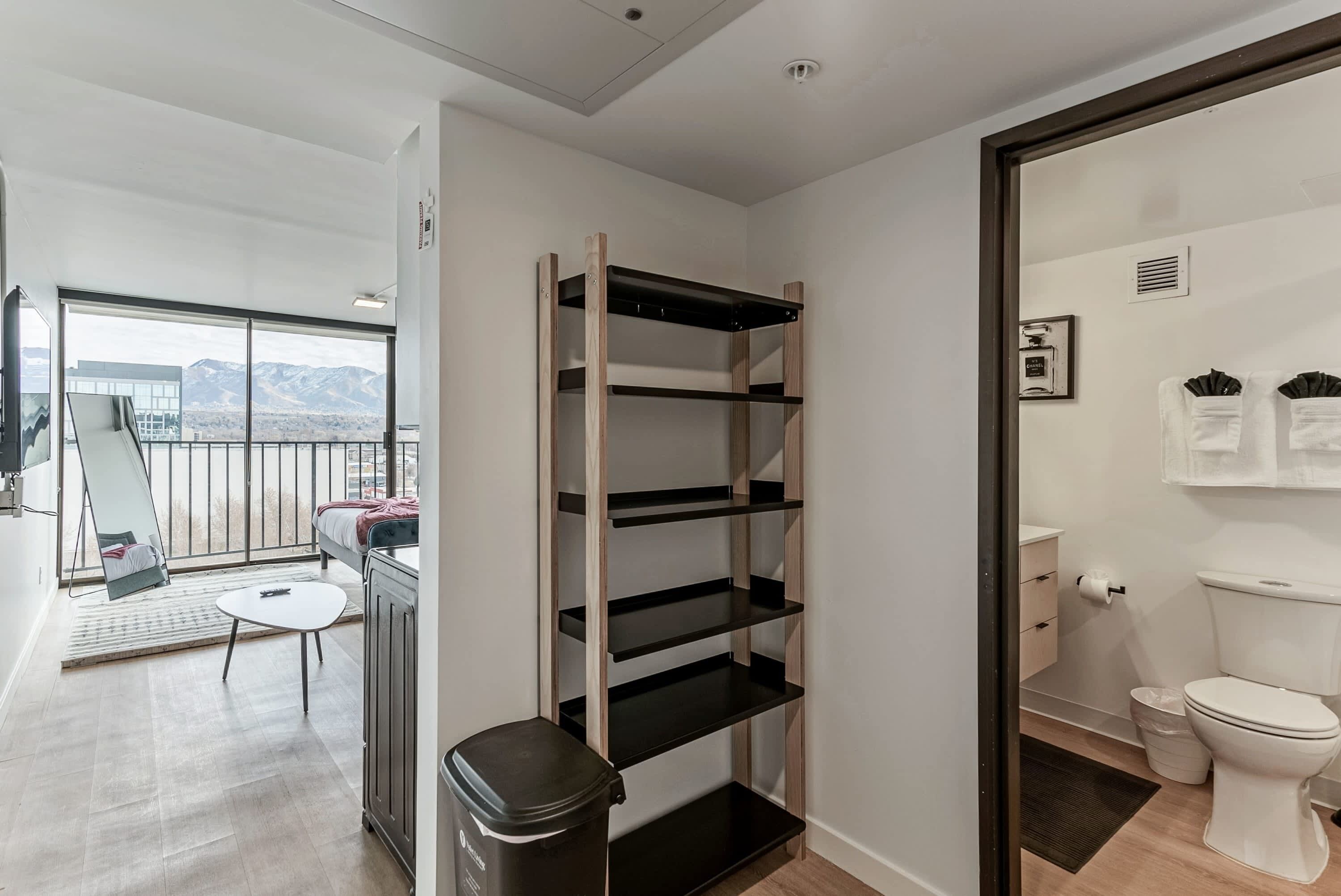 A modern apartment with a balcony, a compact bathroom, and a built-in shelving unit.