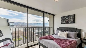 Ein Schlafzimmer mit einer großen Glasschiebetür, die auf einen Balkon führt, einem Bett mit grauem Kopfteil und Blick auf die Berge.