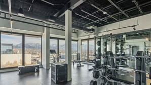 Ein Fitnessstudio mit großen Fenstern, Krafttrainingsgeräten und Bergblick.