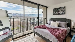 Ein Schlafzimmer mit großem Fenster, einem Bett, einem Nachttisch und einem Gemälde.