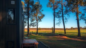 A rustic cabin with a wooden deck and a bench, overlooking a grassy field and trees. - Coleslea by Tiny Away (Leeton)