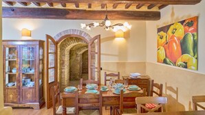 A dining area with a wooden table set for four, a brick archway, and a fruit painting on the wall.