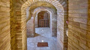 A narrow stone corridor with arched brick walls and a wooden wine rack at the end.