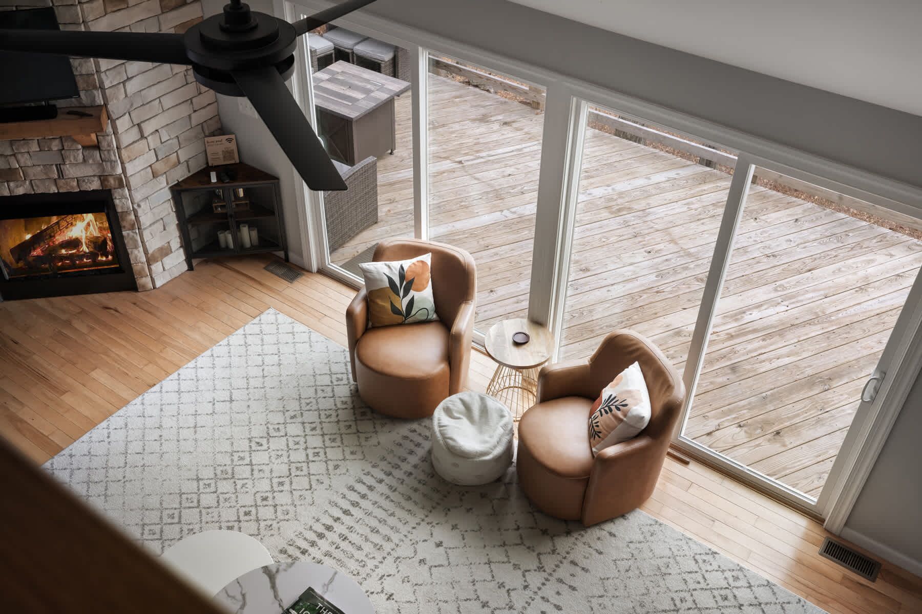 A cozy room with a fireplace, two leather armchairs, a small round table, and a view of a wooden deck through large windows.
