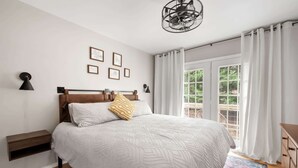 Een slaapkamer met een groot bed, een houten hoofdeinde, een bankje, een kamerbreed tapijt en uitzicht op groen buiten het raam.
