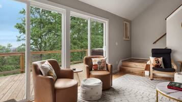 Amplia sala de estar con ventanas grandes, una terraza de madera y vista a árboles.
