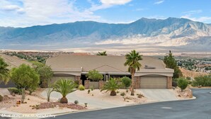 A modern house with a large driveway, surrounded by desert vegetation and mountains in the background. - Luxury, 4+ Bedroom, 4 Bath Home on Golf Course with the Best View in Mesquite! (Mesquite)