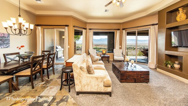 A spacious living room with a large sofa, dining table, and chairs, a ceiling fan, and large windows offering a view of the outdoors. - Luxury, 4+ Bedroom, 4 Bath Home on Golf Course with the Best View in Mesquite! (Mesquite)