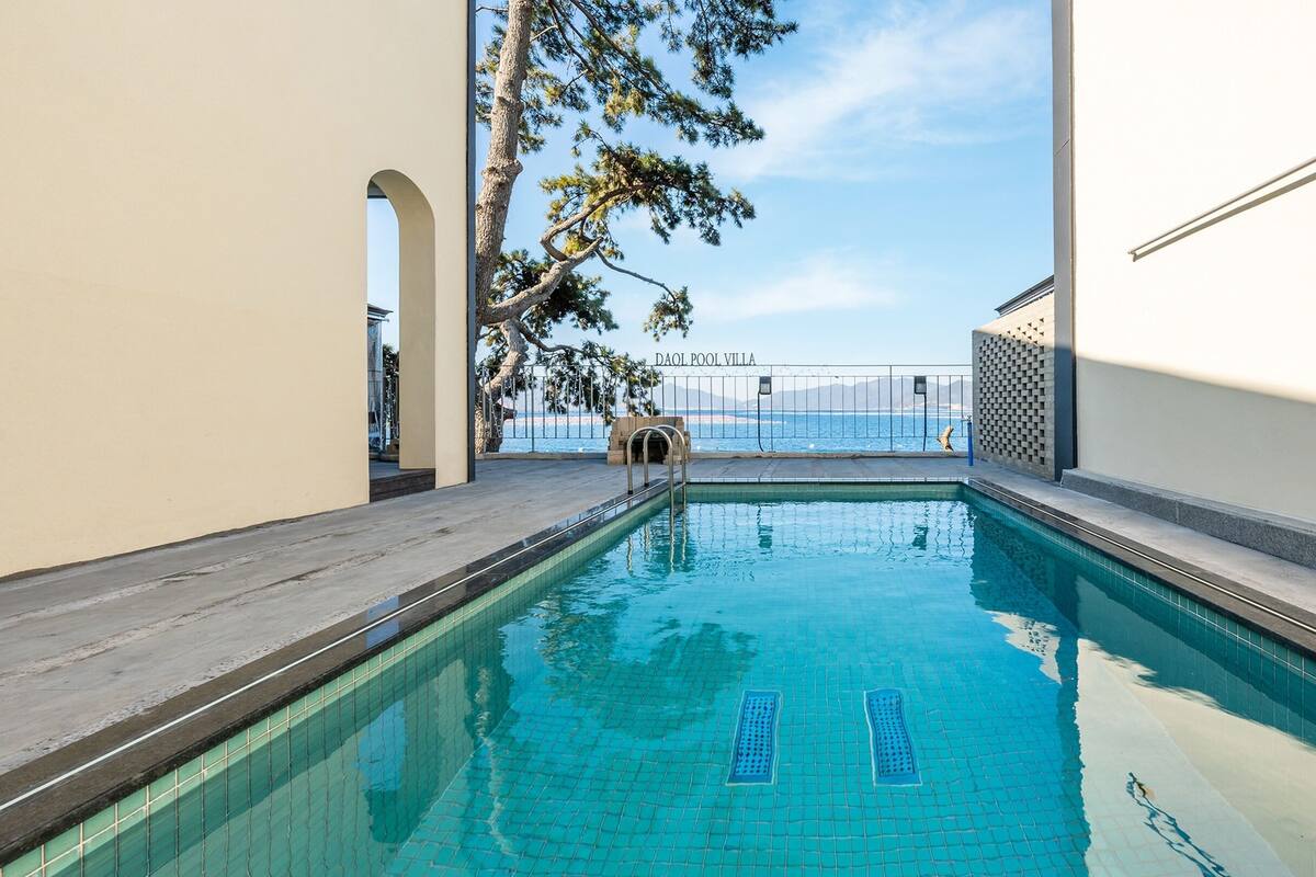 A swimming pool with clear blue water, a view of the sea, and the text "DAOL POOL VILLA" on the wall.
