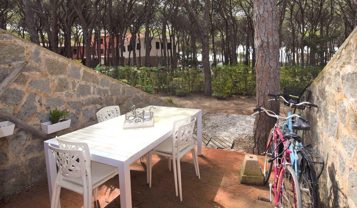 An outdoor patio with a stone wall, a white table, and chairs. A bicycle is parked against the wall.